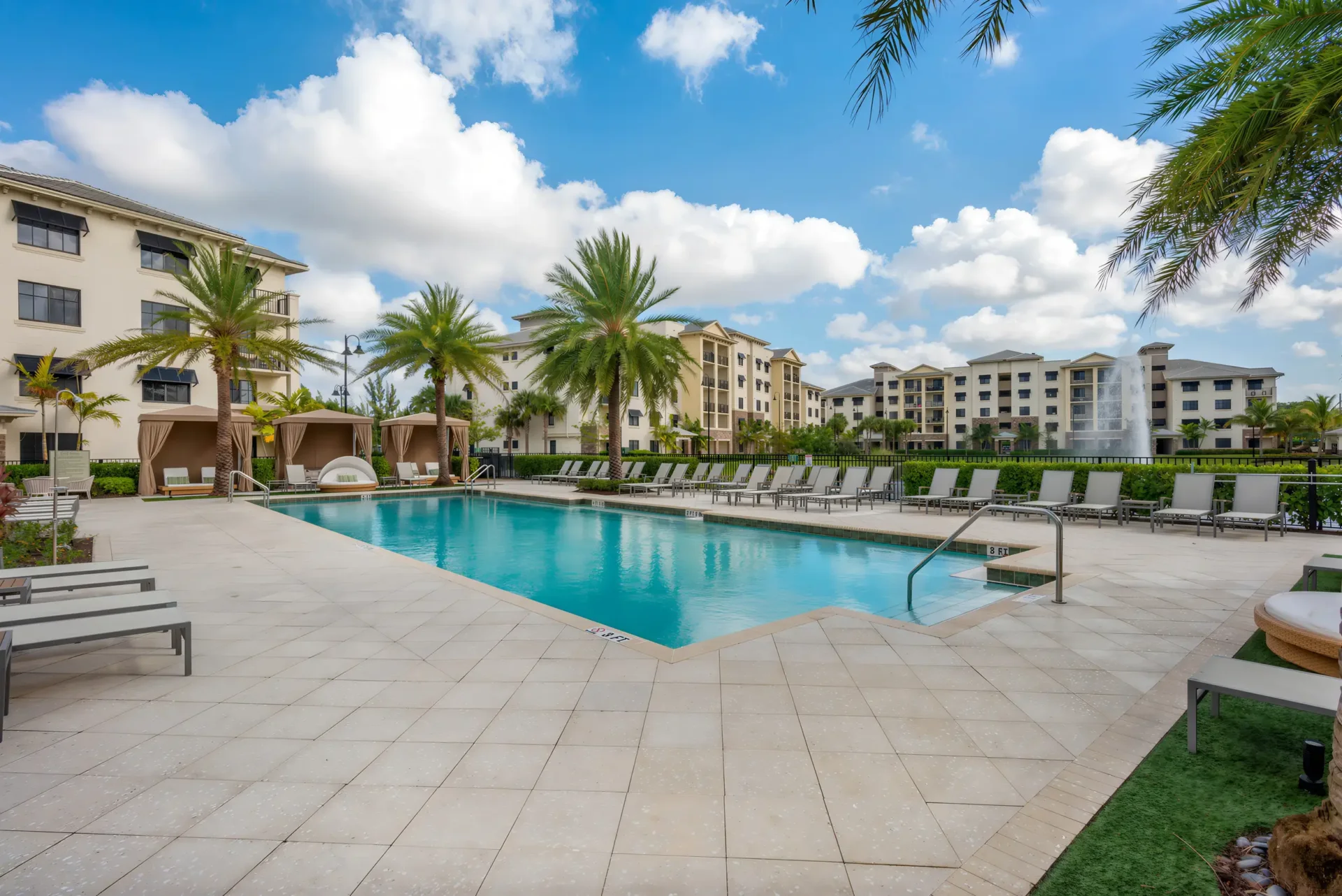 A sun-drenched lakeside pool area with stylish lounge seating and a view of the modern 1, 2, and 3-bedroom apartment homes at The Ellery.